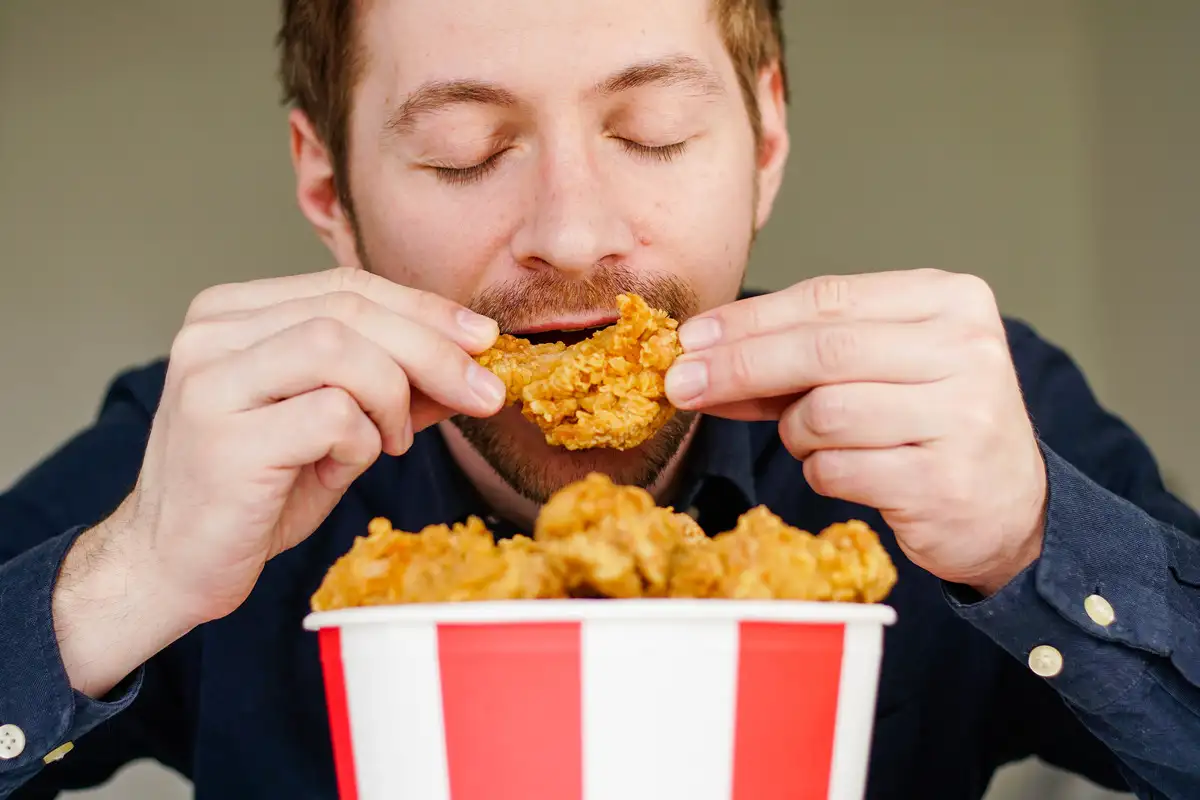 Hungry excited guy eating fried chicken wings