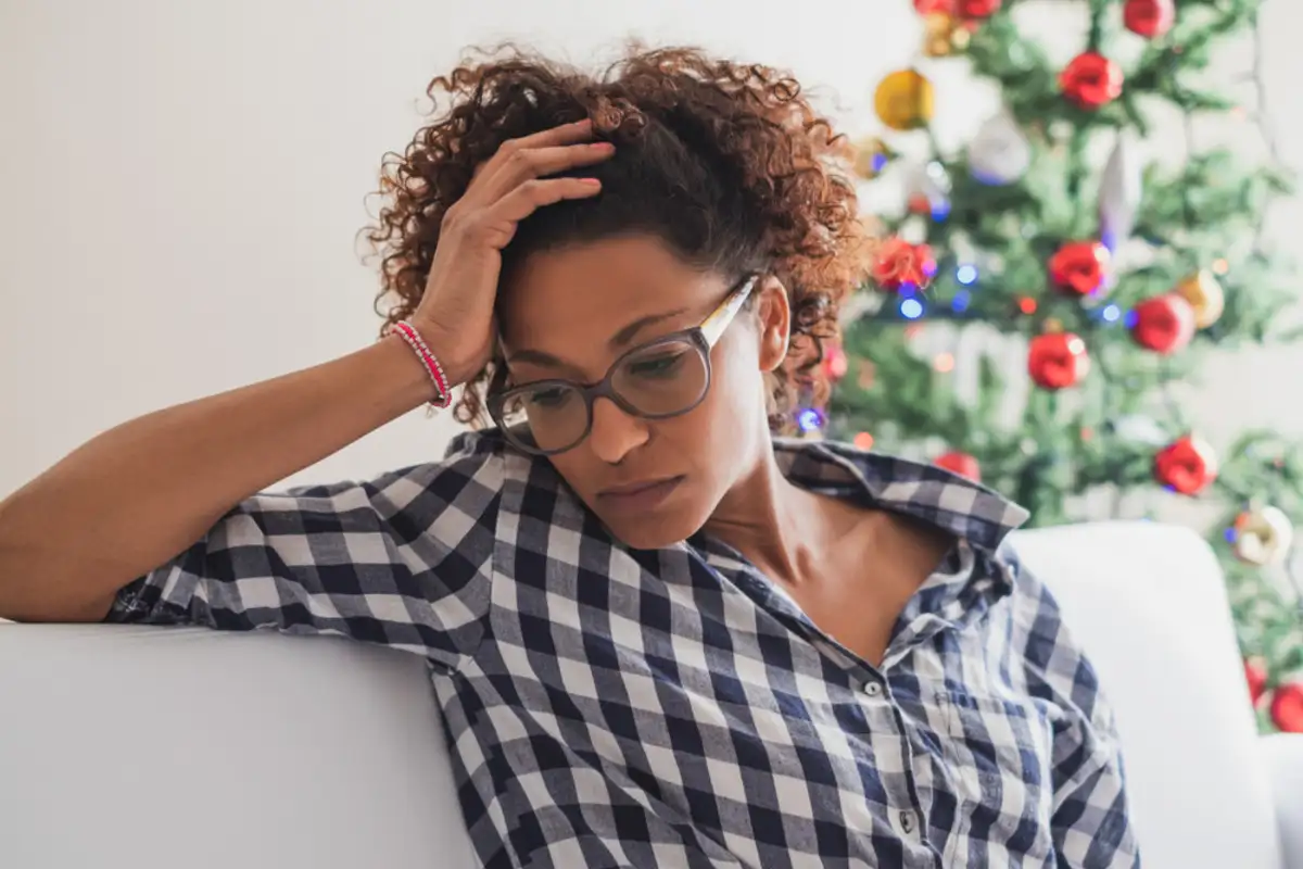 Woman sitting on a couch feel depressed in front of a christmas tree