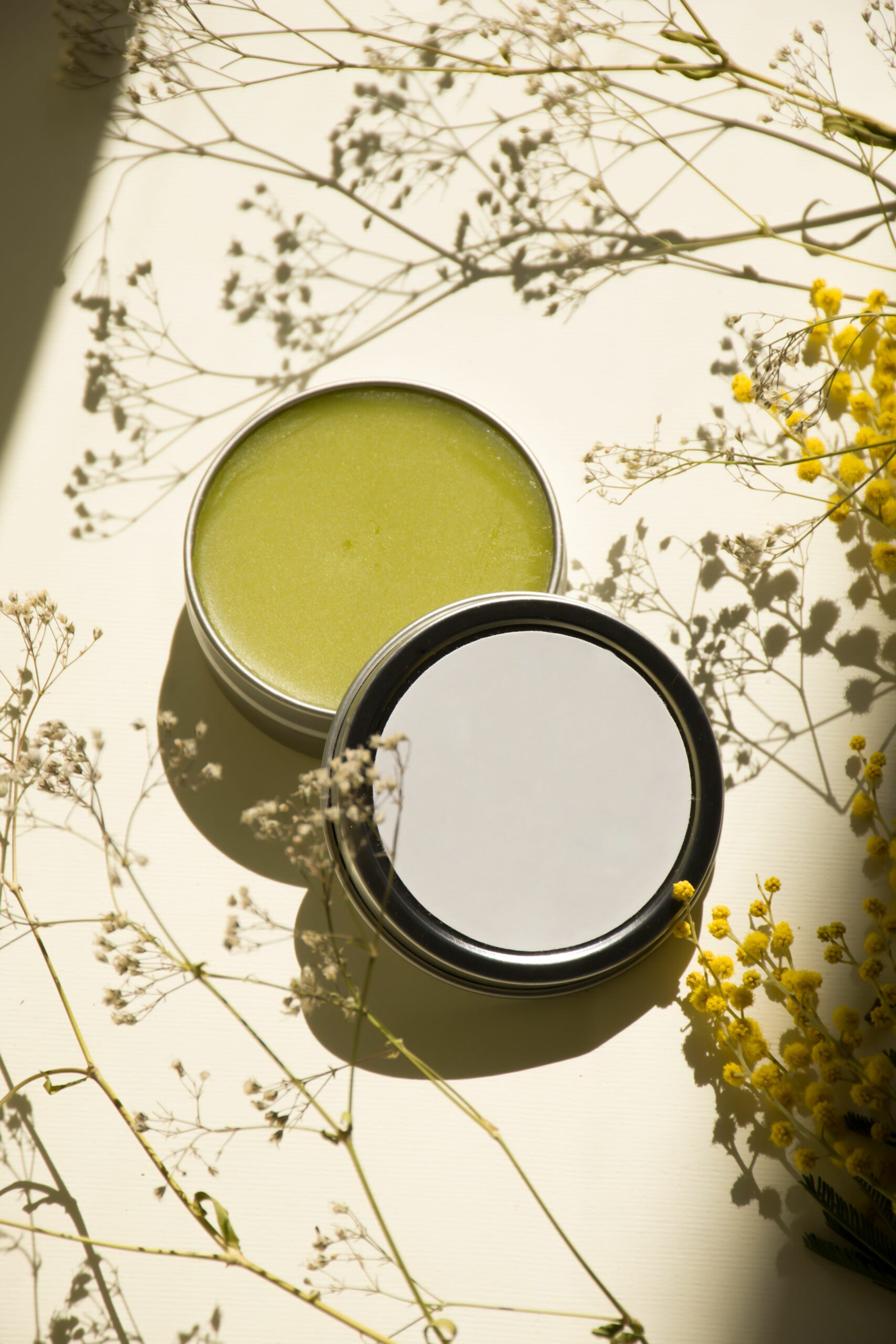 Silver tin filled with green balm on a table with small flowers